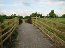 Footpath between post-and-rail fences rising to meet wooden footbridge across Jubilee River.
Path continues up hill in the distance towards large trees.