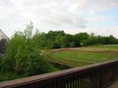 Jubilee River with footbridge railing in the foreground.
High fence around paper yard on the left.
Field and trees on the right.