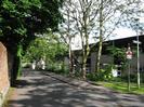 Looking East on Rectory Road.
High brick wall on the left with trees overhanging.
Traffic-calming hump in road.
Cedar Chase houses on right with trees and shrubs between them and the road.
Roadsign and streetlight.