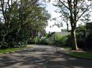 The entrance to Cedar Chase.
Large trees on both sides of the road.
Houses on the right.