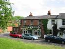 The Oak and Saw public house.
Red brick building with dark slate roof.
White-painted house to the right.
Parked cars.
Part of Village Green in foreground.