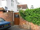 Entrance to Old Lodge West and Old Lodge.
Brown-painted door in high red brick wall.
Pink painted house with tiled roof and scaffolding tower.
Parked car.
Estate-agent's sign.