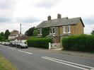 Road with parked cars.
Houses and bungalow.
Telephone pole.
Hedge with white wooden gate.