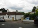 White bungalow with dark tile roof.
Parked cars on road.