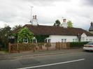 White bungalow with dark tiled roof.
Wooden picket fence.
Road and footway.