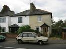 Group of houses, white painted with dark slate roofs.
Low brick wall alongside road.
Parked cars.