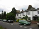 White painted houses with dark slate roofs.
Trees and shrubs in front of some houses.
Road with parked cars.
Telephone pole.