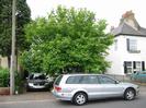 Road with parked car.
Houses with driveways and trees.
Telephone pole.