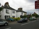 Road with parked cars.
Group of white-painted houses with dark slate roofs.
Roadsign on right warning of new traffic island.