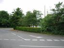 Road junction.
Hedge and trees on far side partly obscure block of flats.
Road sign and telephone pole.