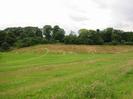 Grassy slopes down to area of rough grass.
Trees at the top of the far slope obscure Station Road.