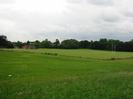 Rough grass area with playing field beyond.
Trees and club-huts in the distance.
Cellphone tower on the horizon.