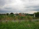 Rough grass with row of low posts.
Road beyond posts, with fence and allotments on the far side.