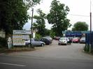 Entrance to trading estate.
Signs on left advertising car repairs and other services.
Parked cars.
Low building with PARKFORD over the door.
High blue metal fence on right.