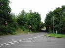 Looking south on Hitcham Road.
Embankment with trees and bushes on left.
Roadsign warning of height restriction.
Traffic lights.
Narrow railway bridge.
Streetlight and control-box for traffic lights.
Large trees in front of railway on right.