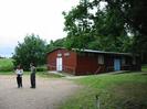 Wooden club-hut set among trees.
Gravel car-park with people.