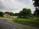 Sports club building and playing field.
Road, grass verge, wooden fence, small trees.