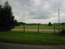Grass verge, chainlink fence, playing field beyond with rugby goals.