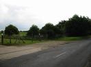 Entrance to sports club.
Concrete and gravel area beside road.
Chainlink fence.
Trees on the right.