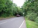 Looking north on Station Road.
Trees on both sides overhanging road.
Parked cars on the left.