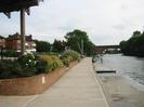 Looking south along the bank of the Thames, towards Brunel's famous railway bridge.
Blocks of flats visible on the left across car-park.
Old boatyard crane at end of quay, with large trees beyond.
Concrete pontoons with boy fishing.
Guards Club Island on the right with large trees.