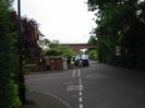 Junction of Ellington Road with River Road.
Trees and houses on left.
Postboxes and noticeboards at junction.
Cars parked on River Road.
Railway bridge in the distance.
Roadsigns for 10mph speed limit, no-through-road, road humps, private road.