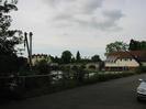 Maidenhead Rowing Club with Maidenhead Bridge and Thames Riviera Hotel to the left.
Road in foreground with wooden railings.
Old boatyard crane in car-park.