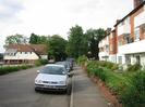 Looking north on River Road.
Maidenhead Rowing Club on left.
River Court flats on right, with gardens and low brick wall.
Parked cars.
Trees in distance at junction with the A4 Bath Road.