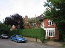 Rosemead.
Red brick house with dark roof and white-painted woodwork.
Wrought-iron balcony.
Hedge and fence along road, with telephone pole.
Parked cars.