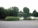 Car park with River Thames beyond.
Large black and white house on far bank.
Trees on Guards Club Island and on far bank.