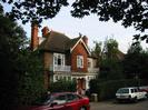 Thames Bank.
Red brick house with white-painted woodwork.
Partly tile-hung at first-floor level.
Dark tile roof with decorative figureof a dragon on gable-end.
Cars parked in road.