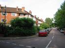 Ellington Road.
River Court flats on the left, with bushes in front.
Antique-style street lamp.
Parked cars.
Trees on right of Ellington Road.