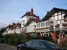 Gaiety Row houses.
Many colourful hanging baskets.
Hedges and walls along road.
Parked car.