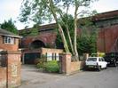 House and garage on left.
Railway bridge behind tree on right.
Parked cars on road.