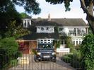 Kingfishers: large house with white-framed windows and dark tile roof.
Wrought-iron gates to driveway, with overhanging trees.