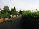 Looking south on River Road.
Walls and gates on left.
Bushes on right.
Cyclist on road.