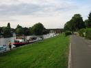 River Thames with moored boats.
View through mainline railway bridge to Maidenhead Bridge beyond.
Grassy bank between river and road.
Trees in the distance.