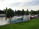 River Thames with moored boats.
Grassy bank.
Trees and houses on far side of river.