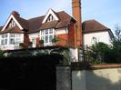 The Riverbank House seen across high hedge.
White-painted woodwork. Partly tile-hung at first floor level.
Red tile roof with small windows set into gable ends.
Iron railings around first-floor patio.