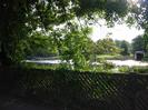 Low wooden fence with trees and view of River Thames.
Small boathouse on far bank.