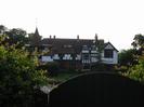 Wooden gate with River Thames beyond.
Large black and white house on far bank.