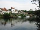 River Thames, with Gaiety Row houses on the far side.
Most houses are white painted with some black timbers, and have red tile roofs.
Steep gardens lead down to the river.
Moored boats.
Railway embankment on far right.