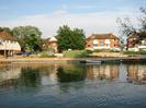 River Thames.
Pontoon and boats against the far bank.
Rowing Club building on left.
Car park with cars and boat trailers.
Houses and flats on River Road in the background.