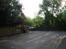 The junction between Ellington Road and River Road.
Trees and wooden fence on left, with post-boxes and notice boards.
Road signs on the far side of River Road, against bank of trees.