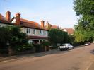 Road with parked cars.
Houses on far side have long porches are rendered at first-floor level, and have red tiled roofs.