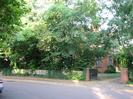 Road and pavement with wooden fence and overhanging trees.
Driveway between brick pillars with black wooden gate.
House just visible through gate.