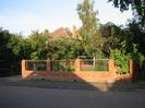 Brick wall with inset ironwork sections in black and gold.
Sign on wall: "BYWAYS"
Driveway on left.
Small trees in garden behind wall.
Roof and chimneys visible over trees.