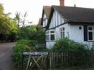 White bungalow with black timbers and white bay window.
Dark tile roof.
Low wooden paling fence.
Street-name sign for Ellington Gardens.