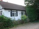 Rowan Trees: white bungalow with black timbers and dark tile roof.
Low wooden fence.
Trees on right.