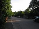 Road with parked cars.
Pavement and low walls on left with trees overhanging.